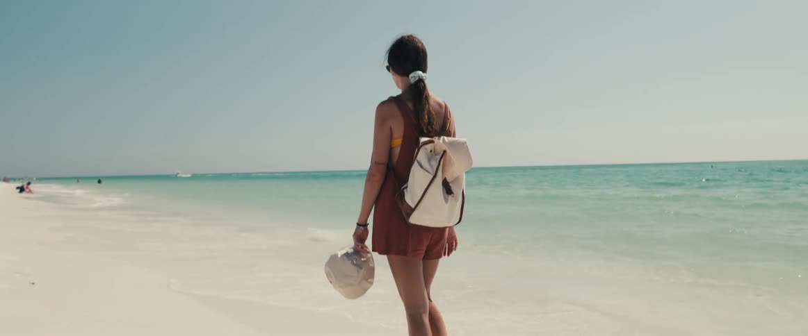 A teenage girl walking down the beach towards people sitting on the beach