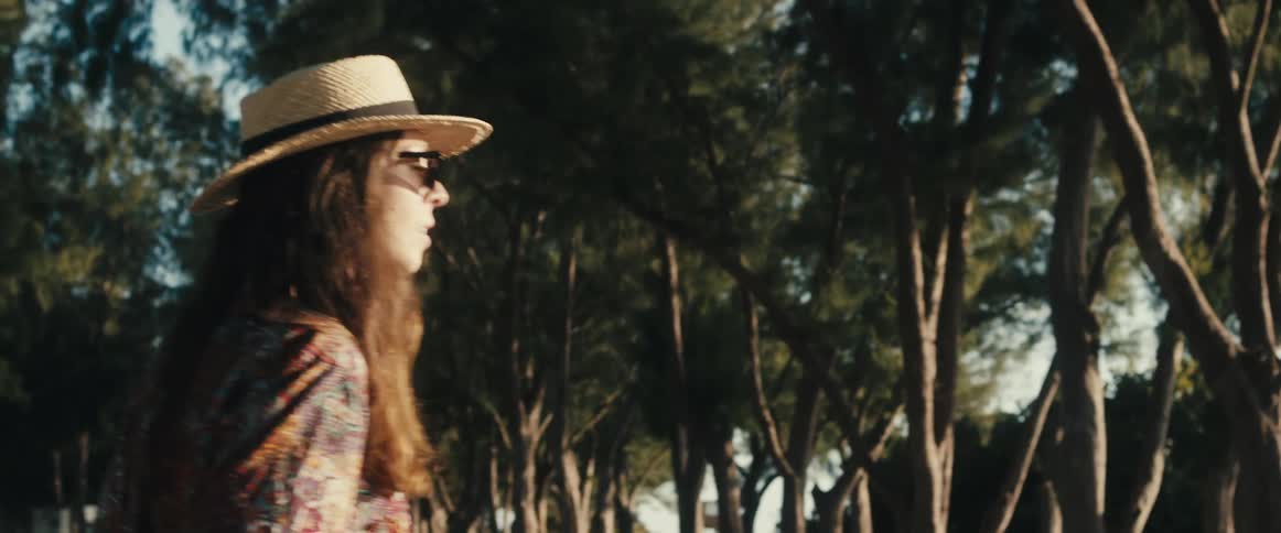 A woman in a sun hat and sunglasses looks around a public park