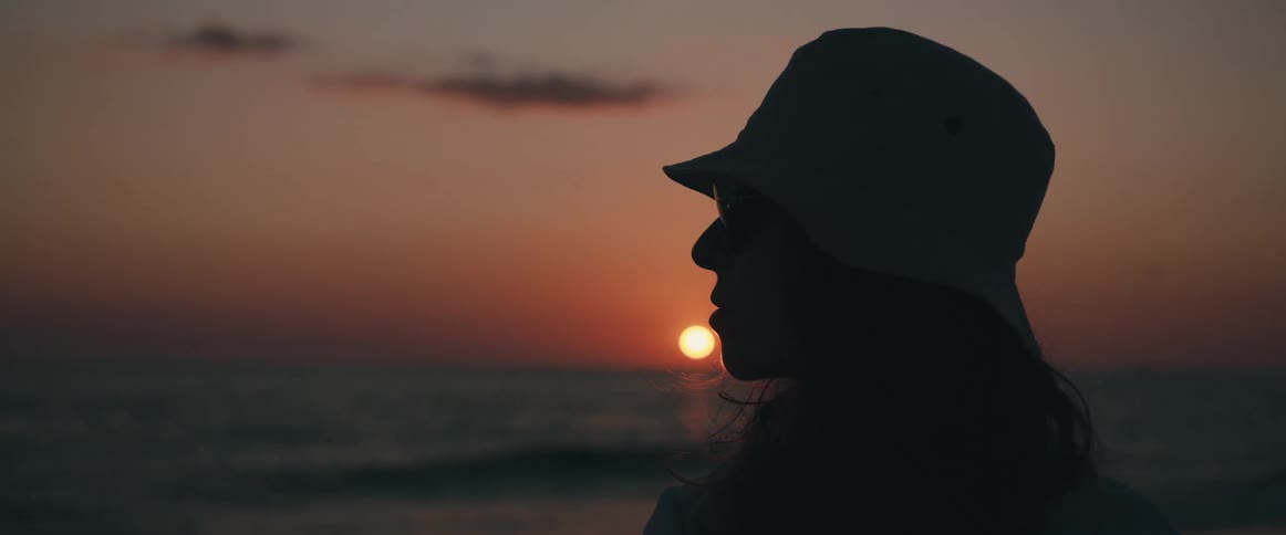 A female standing near the ocean looking towards the horizon