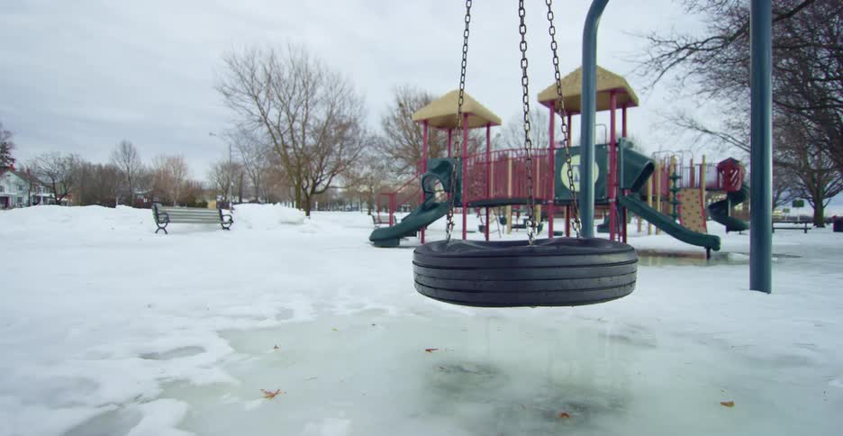 A tire swing blowing in the wind in a park on a winter day