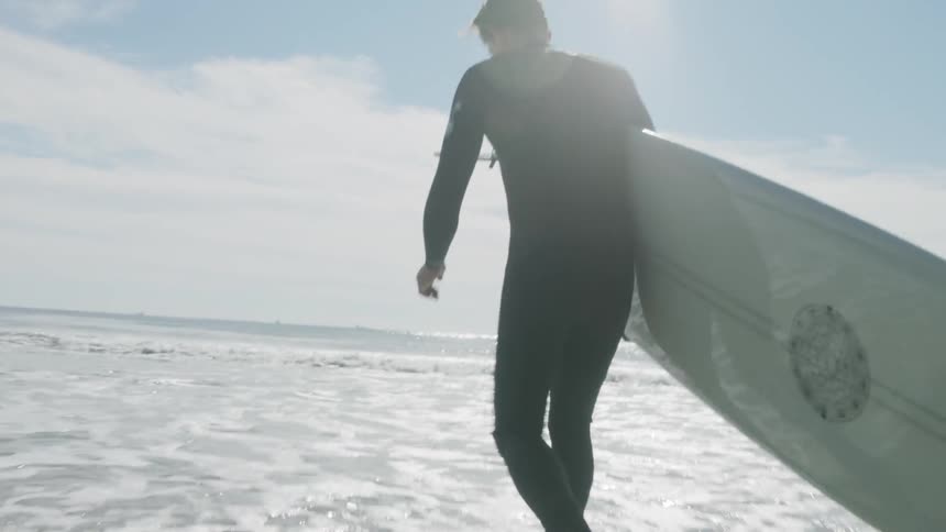 A man carries a surfboard into the ocean