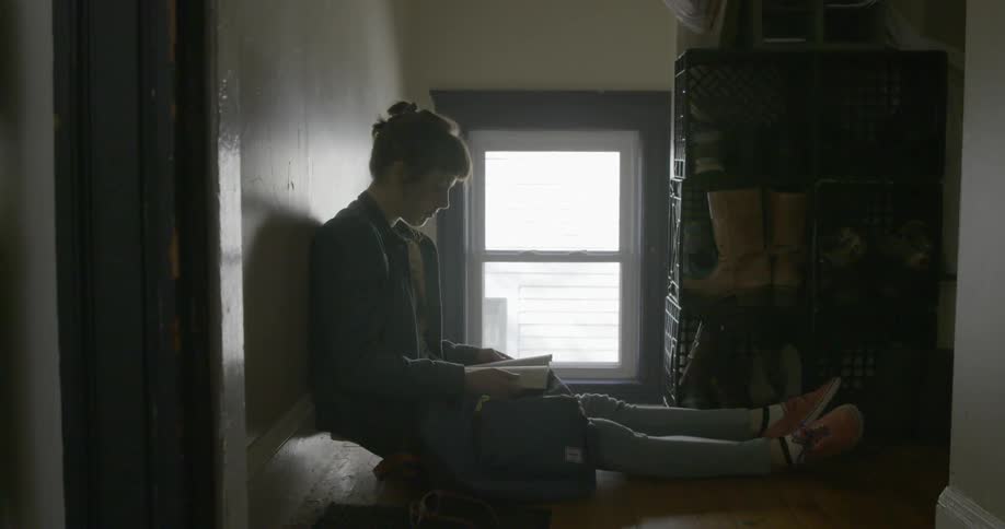 A woman sits next to a window reading a book