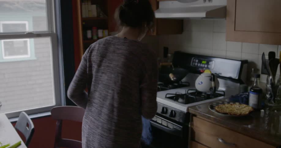 A woman sits down at a kitchen table and uses a phone