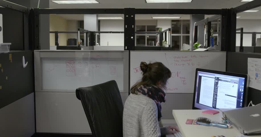 A woman is sitting at a desk staring at a monitor