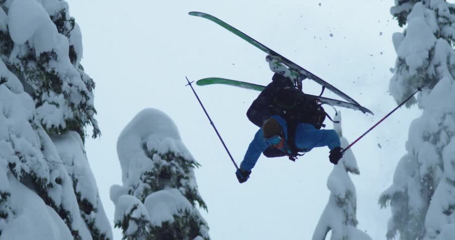A man does a flip while skiing down a mountain