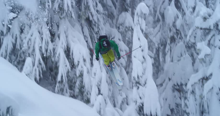 A skier jumps and spins over an old tree trunk in the deep forest
