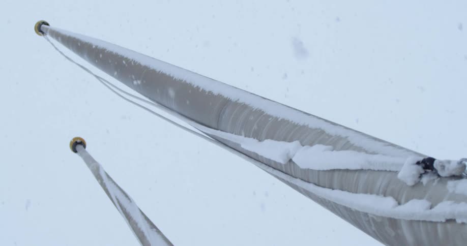 Snow falls past flagpoles with ice crusted ropes