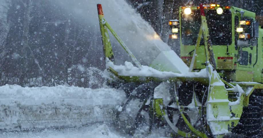 A heavy duty snow plow throwing snow off a street