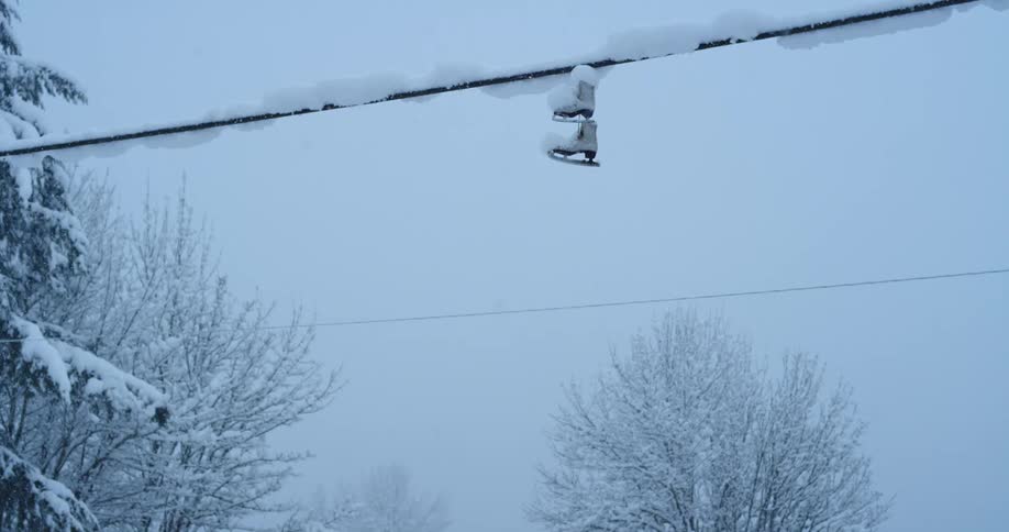 Snow falls on ice skates hanging from a telephone wire