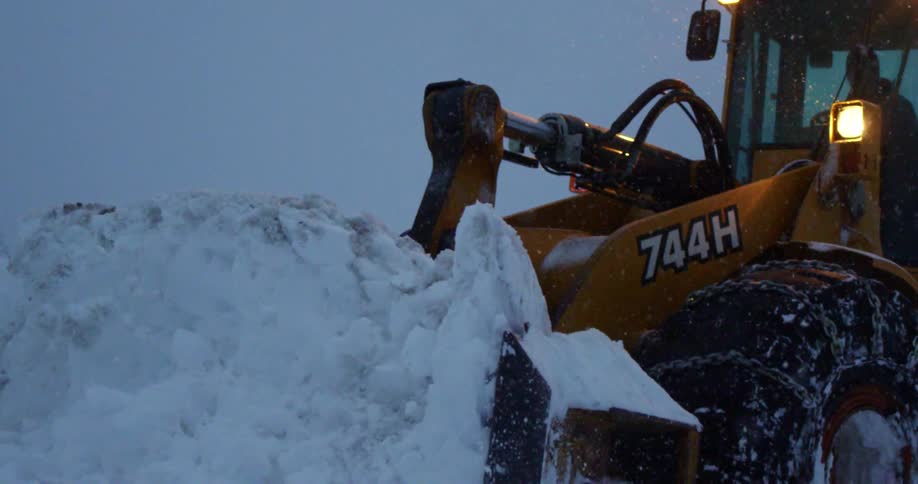 A man driving a snowplow pushes a large amount of snow