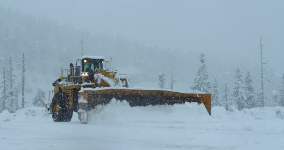 Heavy machine pushes a huge snow plow down a road in a snow storm
