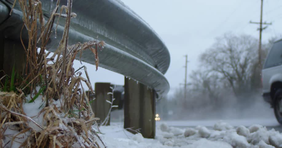 A metal guardrail runs alongside a road that is covered with snow and ice