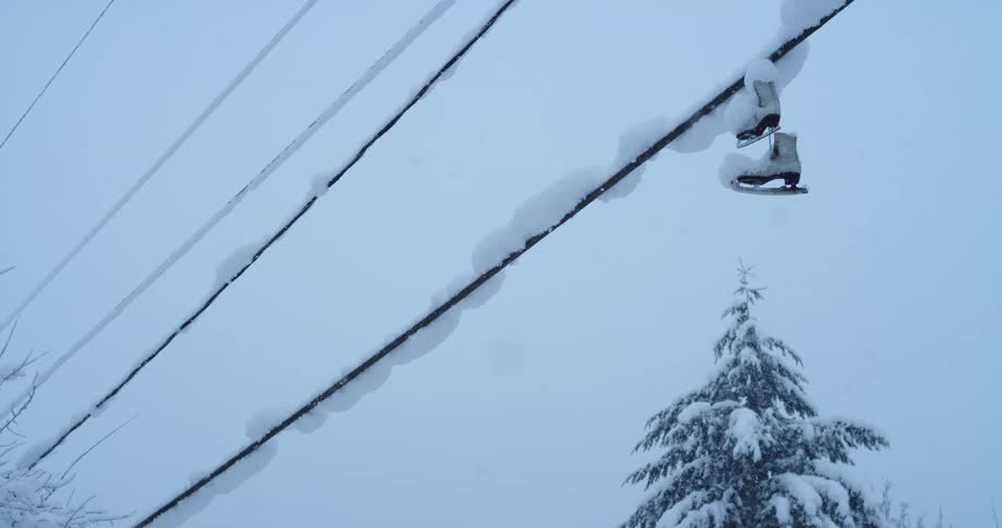 A pair of white ice skates are dangling off a black powerline on a cold snowy day