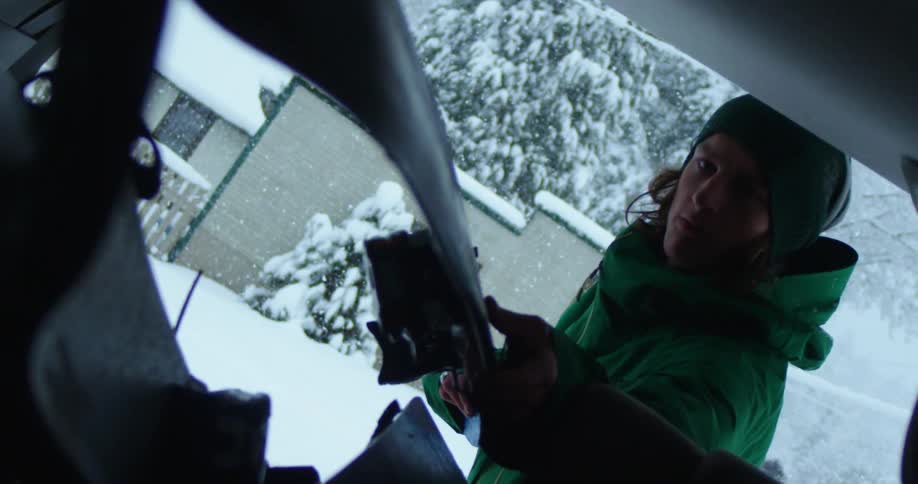 A man places a ski in the trunk of a vehicle while standing outside in the snow