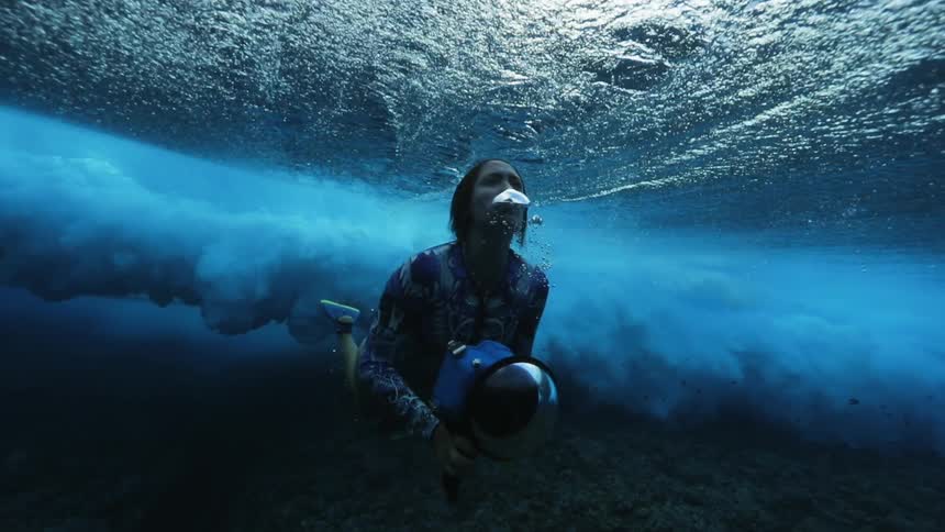 A huge wave rolls over a woman holding an underwater camera