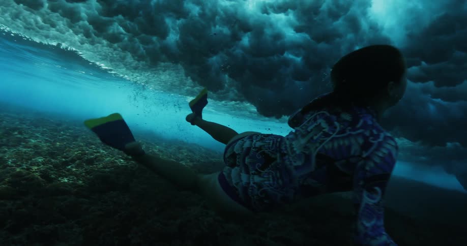 A woman dives down under the surface of the ocean as a roiling wave passes overhead