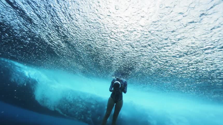 A woman is swimming underwater as a wave washes her away from the camera