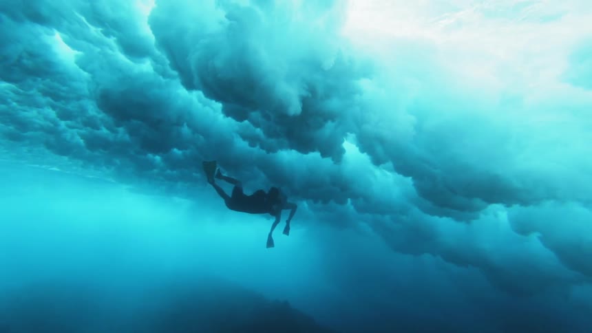Swimmers diving underwater with waves overhead