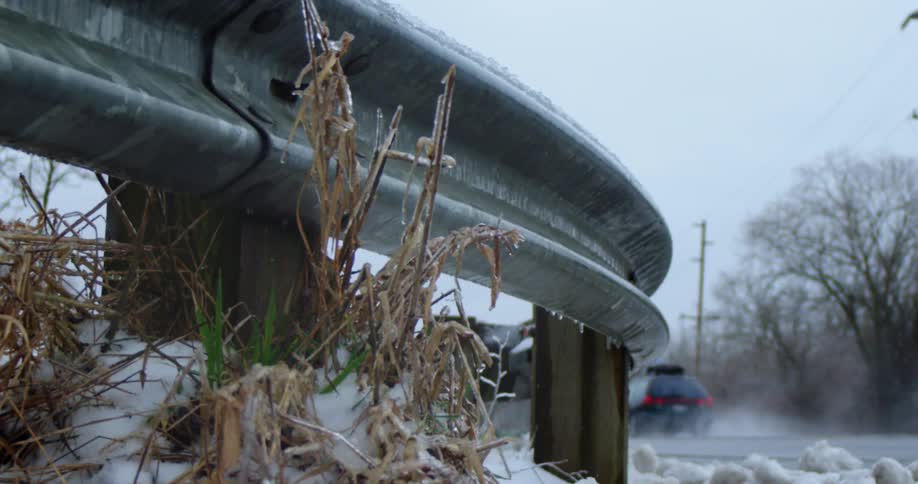 Water splashes as a black station wagon drives down a road in freezing rain