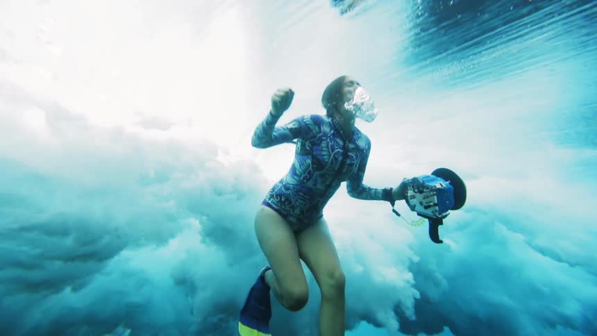 A huge wave crashes over a woman filming underwater