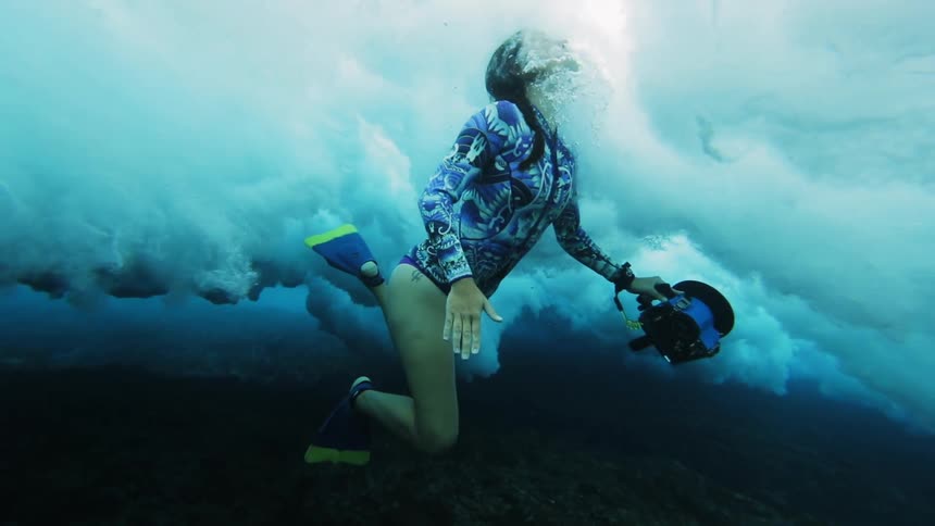 A woman is swimming up from the ocean floor into a large surface wave