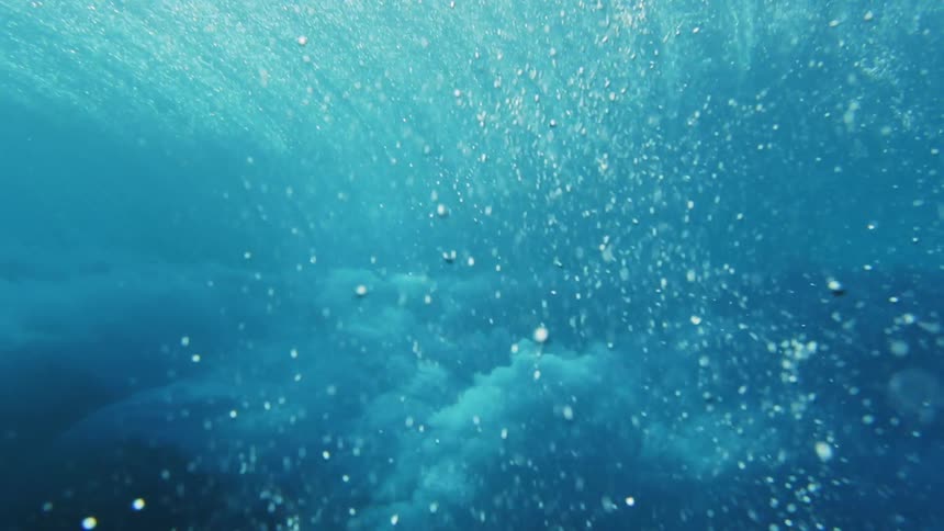 An ocean wave illuminated by sunlight crashes causing a cloud of bubbles to form underwater