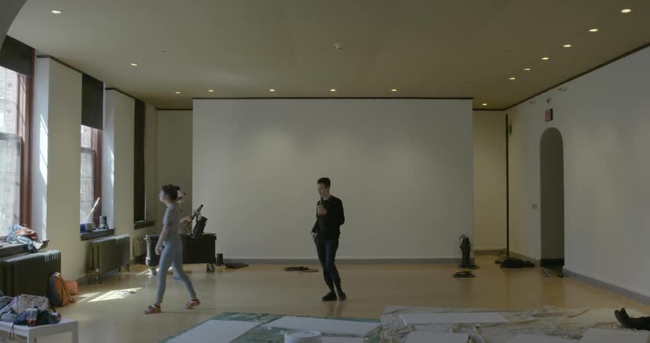 Two people walk across a floor with a woman standing on the side