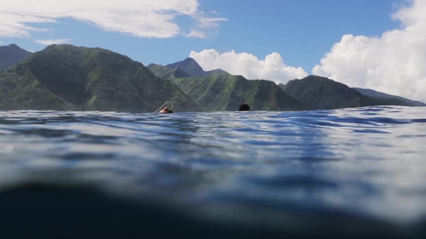 Surfer floats on a surfboard on the surface of the blue ocean waters near the coastal mountains