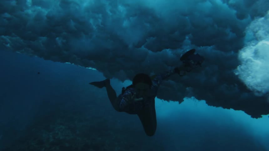A woman swimming under water as large waves crash above her
