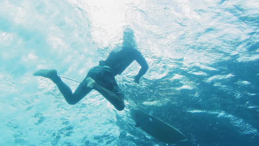 Underwater view of a man treading water by his surf board