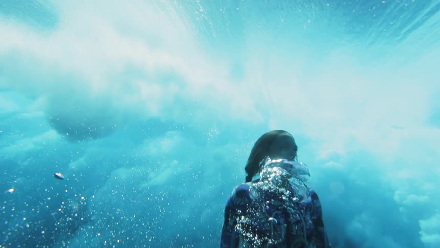 A woman dives under a roiling wave underwater