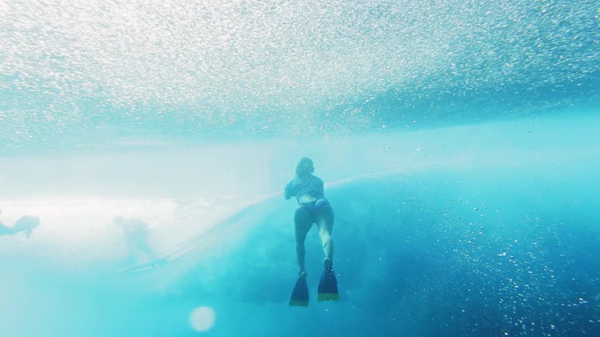 A female diver with an underwater camera films a passing surfer underwater