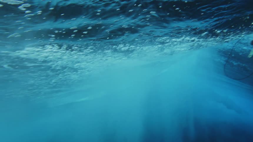 Under water footage of a man surfing as a wave crashes overhead