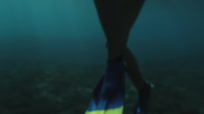 A white woman in a blue bathing suit is snorkeling above a reef on the ocean floor