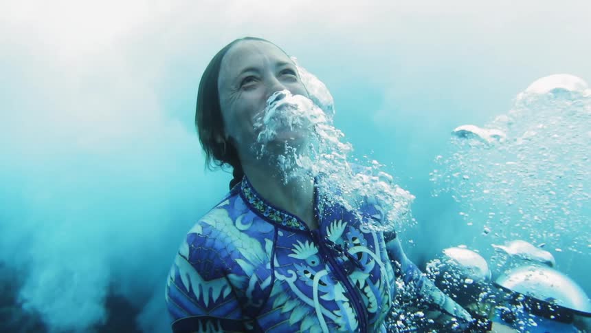 Woman rises toward surface of ocean flowing bubbles and smiling