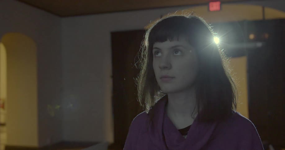 A woman stands staring at something inside a large room