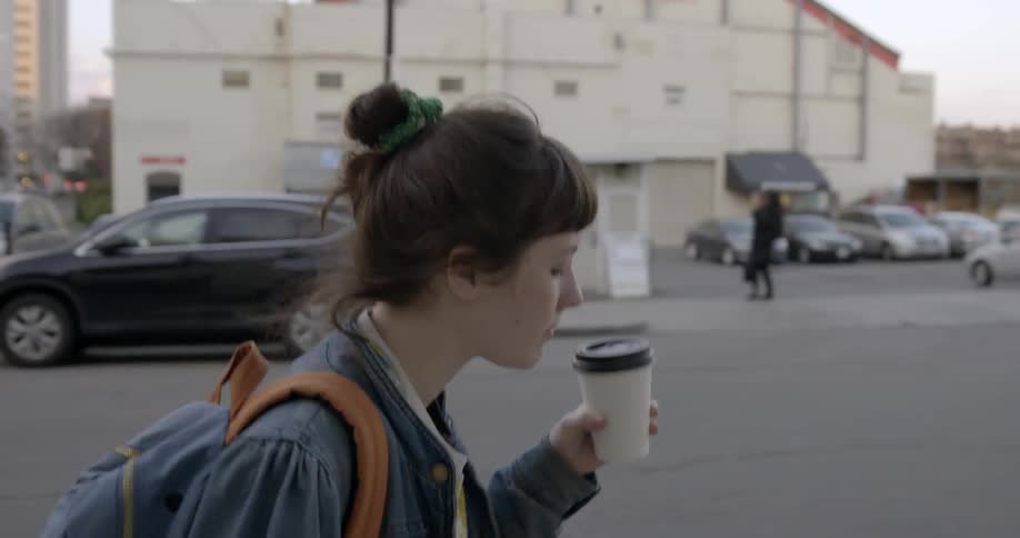 A woman is walking outside drinking from a cup