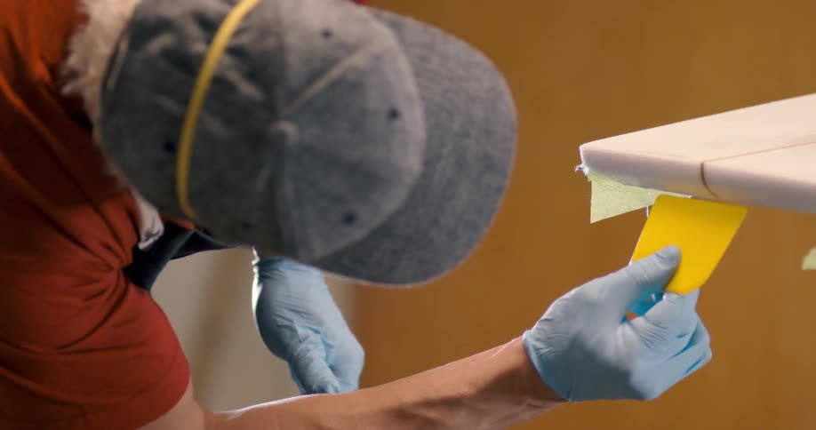Man smooths the surface of a surfboards edge in the workshop