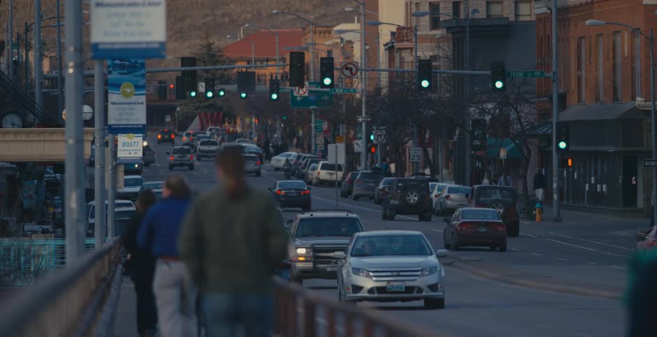 Pedestrians walk a city sidewalk as vehicles travel by