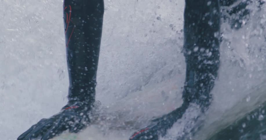 A person with a wetsuit laying on a surfboard then standing with water splashing