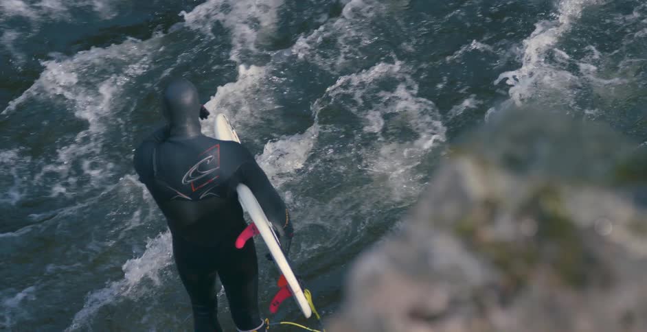 A surfer in a wet suit standing next to water rapids