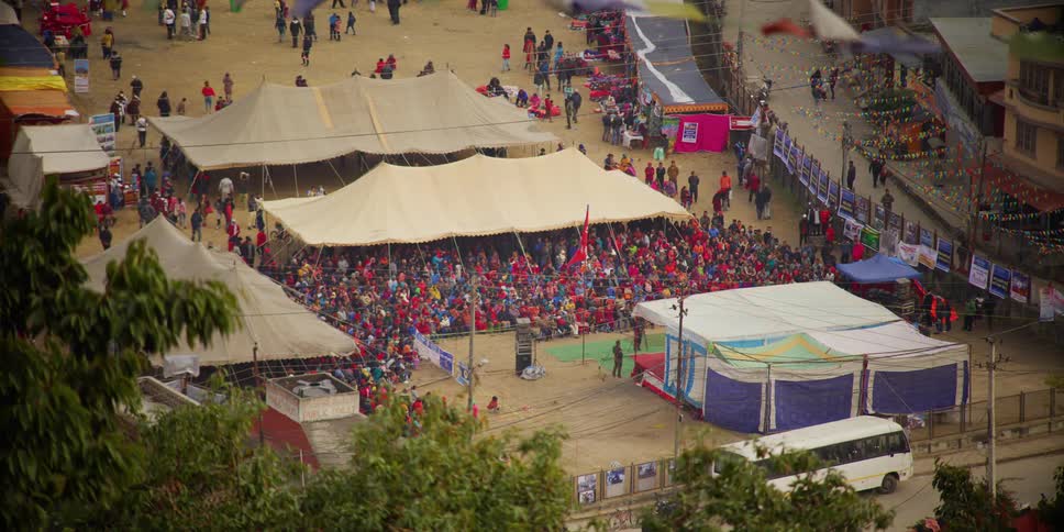 People crowd under and near a large outdoor tent at a festival in a developing country