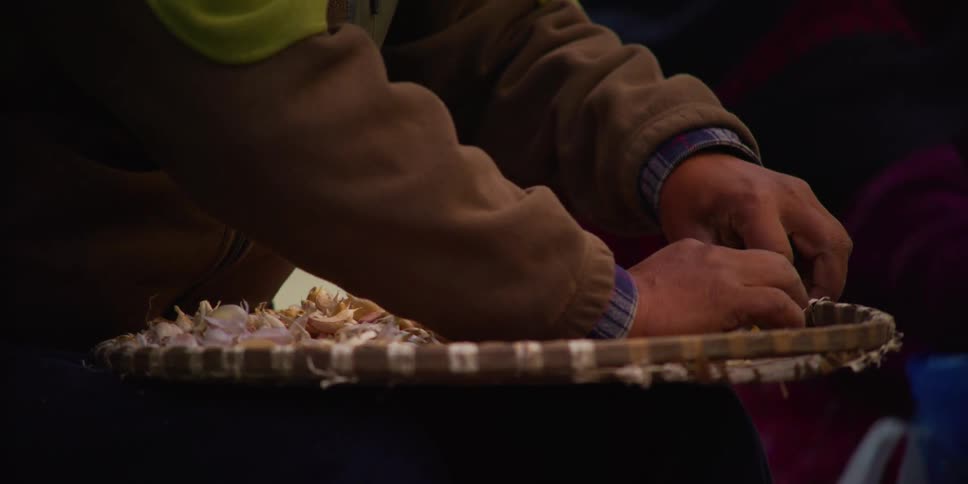 A man quickly separates shallots on a large bamboo tray
