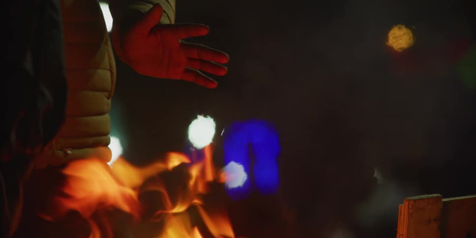 People warming themselves next to a bonfire at night