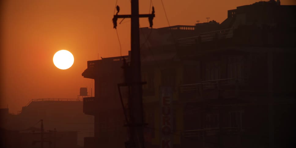 Silhouetted city buildings in front of an orange sky and sun