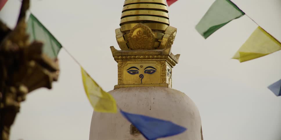 A statue with a face and gold in a windy area near flags
