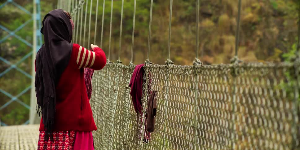 A woman flaps a wet shirt in her hands to straighten it as she stands next to a chainlink fence with wet clothing hanging from it
