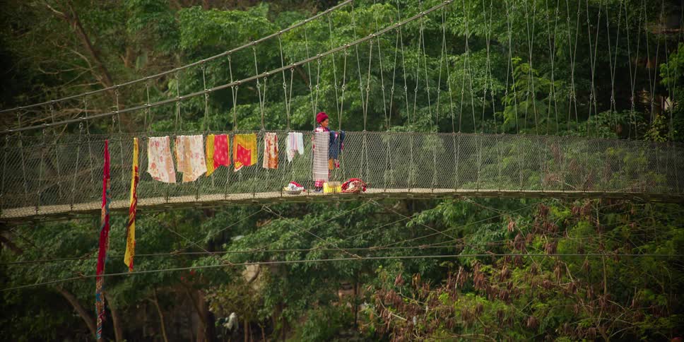 A person on a bridge hanging clothing with trees in the background