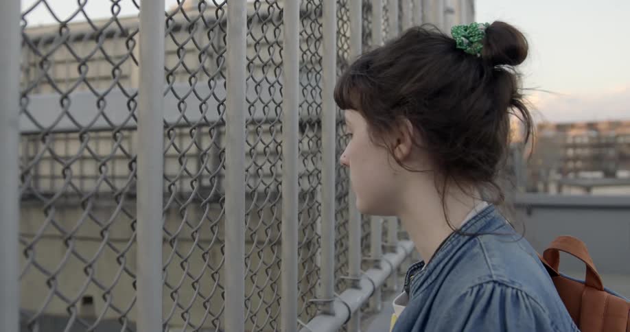 A woman is on a rooftop looking through a fence below