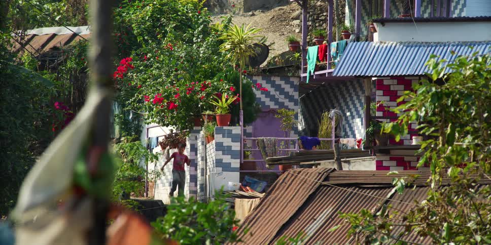 A boy running and jumping surrounded by trees plants flowers and buildings